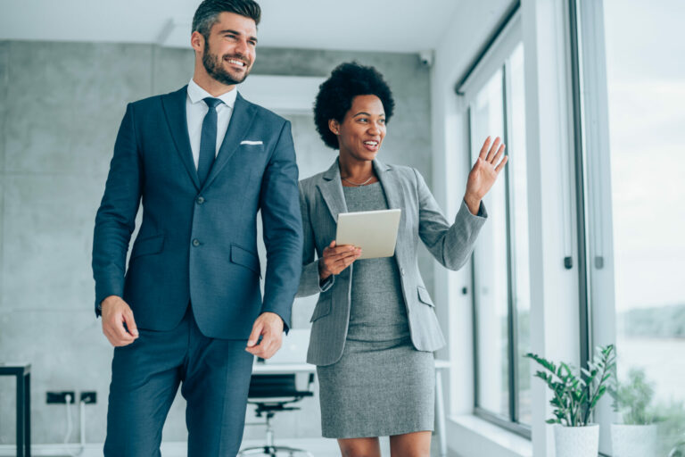 Job 101: Die richtige Kleiderwahl für Vorstellungsgespräche Shot of a two confident business persons talking in the work place. Two colleagues using a digital tablet while walking in a modern office. Businessman and businesswoman in meeting discussing business strategy. Business coworkers working together in the office.