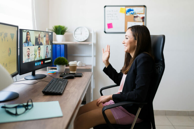Die Herausforderungen der Arbeit im Homeoffice Team work meeting. Happy young woman wearing pajamas and a blazer waving to her co-workers during an online video call from home